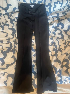 Svarta bootcut kostymbyxor - Snygga svarta kostymbyxor med bootcut passform och pressveck framtill. Byxorna har låg midja, bred linning och dubbla knappar. Perfekta för en stilren look. Materialet känns mjukt och följsamt. Storlek 170 men passar xs/s utan problem. Pris går att diskutera och hör av er vid frågor eller om fler bilder önskas💕
