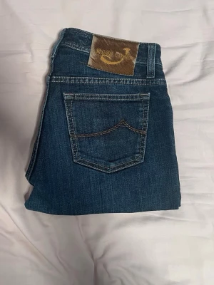 Jacob Cohën  - Snygga mörkblå jeans från Jacob Cohen med klassisk femficksdesign och kontrastsömmar. Jeansens material är denim och de har en läderpatch med logotyp på bakfickan. Perfekt för dig som gillar stilrena och tidlösa jeans.8.5/10 