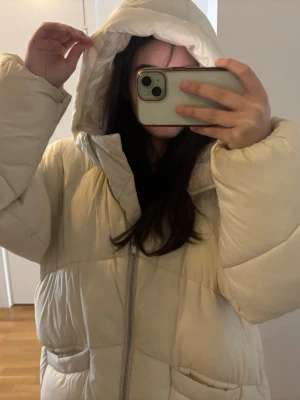 Lång beige pufferjacka med huva - Beige lång dunjacka/pufferjacka från Gina Tricot i storlek M. Varm, bekväm och perfekt för höst och vinter. Snygg oversized känsla och ger en stilren, modern look. Mycket fint skick Säljs eftersom den inte används längre. Skriv gärna om du har några frågor eller vill ha fler bilder 😊