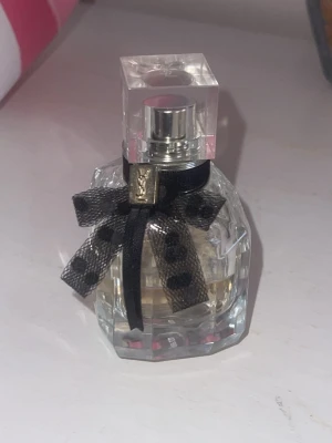 Yves saint Laurent parfym - Snygg parfym från Yves Saint Laurent med en svart rosett och elegant design. Perfekt för dig som vill ha en lyxig touch i vardagen. Halva är använd. 70kr