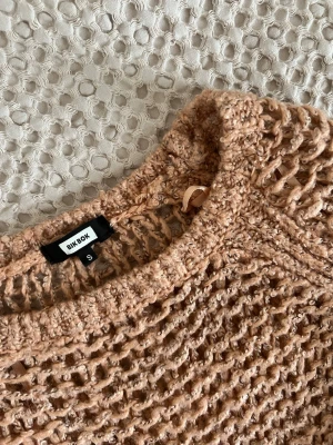 Beige stickad tröja från Bik Bok - Säljer en beige-rosa stickad tröja från Bik Bok i storlek S. Tröjan har ett grovt hålmönster och är långärmad med ribbade muddar vid ärmslut och nederkant. Perfekt för lager-på-lager och ger en cool, avslappnad look.