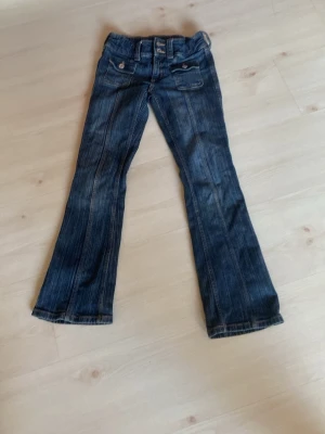 Jeans mörkblåa - Snygga mörkblå jeans med framträdande fickdetaljer och knappar. De har en klassisk bootcut-stil och är perfekta för en avslappnad look. Passar bra till både sneakers och kängor.