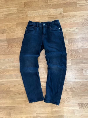 Svarta jeans från Kappahl - Snygga svarta jeans från Kappahl med klassisk femficksdesign och raka ben. Jeansen har knapp och dragkedja framtill samt diskreta sömmar. Perfekta för dig som gillar en enkel och stilren look. Byxorna är i storlek 170/S. Skriv om du undrar något!