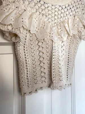 Stickad topp med volang från Zara - Söt vit/crèmefärgad stickad topp från Zara med kort ärm och volang. Tröjan är i storlek S men passar även XS.