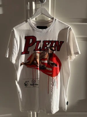 Äkta Vit t-shirt från Philipp Plein - Säljer en vit Limited Edition t-shirt från Philipp Plein med stort rött och svart tryck framtill, där det står 'PLEIN' och en grafisk bild med leopardmönstrad outfit. Klassisk passform och rund hals. Perfekt för dig som gillar statement-plagg och sticka ut från mängden. Nypris 6000kr +