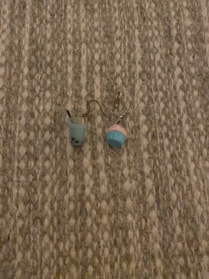 Söta örhängen med boba och cupcake - Unika örhängen i form av en blå boba tea och en blå-rosa cupcake. Perfekta för dig som gillar roliga och färgglada accessoarer. Gjorda i plast med metallkrok. Säljs som ett mixat par för en lekfull stil.