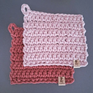 Två virkade grytlappar i ljusrosa och Peony - Två  virkade grytlappar i tjockt repgarn. Tåliga och tvättbara.. Båda har en ögla för upphängning och en liten etikett med texten 'Handmade'. Perfekta som kökstillbehör eller dekoration.