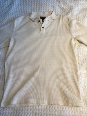 Vit långärmad pikétröja från H&M - Klassisk vit långärmad pikétröja från H&M. Tröjan har krage, knäppning med två knappar och är tillverkad i mjukt bomullsmaterial. Perfekt för en stilren look.