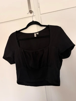 Svart croppad topp med rynkad byst - Snygg svart croppad topp med rynkad byst och fyrkantig urringning. Perfekt till jeans eller kjol för en trendig look. Obs hund finns i hemmet