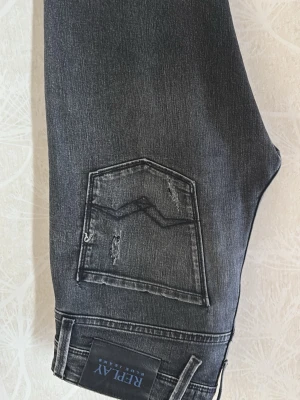 Grå/svarta slitna jeans från Replay - Säljer ett par grå/svarta jeans från Replay med slitningar och distressed detaljer på både fram- och baksida. Jeansen har klassisk femficksmodell och raka ben. Materialet är denim med en snygg tvättad look och coola detaljer på bakfickan.