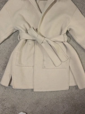 Vit kappa med päls detaljer  - hej! Säljer nu min fina kappa från FUR Stockholm, eftersom den inte kommer till användning längre tyvärr:/ men den är i jätte fint skick använd ett par gånger men typ som ny, (ena bilden är från hemsidan, skriv till mig för bilder på jackan☺️) pris kan diskuteras💓