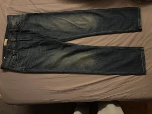Mörkblå jeans från Jack & Jones - Säljer ett par mörkblå jeans från Jack & Jones med klassisk femficksdesign och snygga slitningar på låren. Jeansen har raka ben och är gjorda i ett slitstarkt denimtyg. Perfekta för en avslappnad och trendig look.