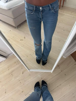 Ljusblå slitna jeans med hål - Säljer ett par ljusblå jeans med raka ben och slitningar på låret samt stora hål vid knäna. Jeansen har klassisk femficksmodell och normal midja. Perfekta för en avslappnad och trendig look. Köpta på Gina i storlek 34