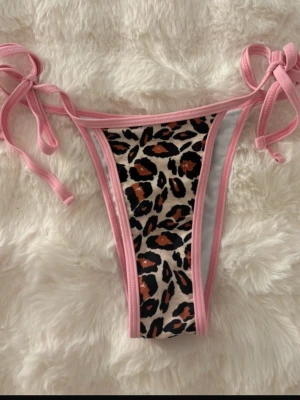 Leopardmönstrad bikiniunderdel XS - Snygg bikiniunderdel med leopardmönster och rosa kanter. Modellen har knytband på sidorna för justerbar passform. Materialet är polyester och elastan, perfekt för sommarens strandhäng. Passar dig som vill sticka ut med coola detaljer och djurmönster.
