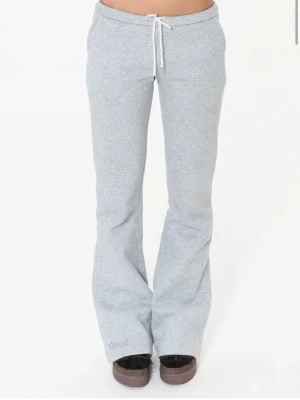 Grå mjukisbyxor från Nitted - Säljer ett par ljusgrå mjukisbyxor från Nitted med utsvängda ben och dragsko i midjan. Byxorna har en relaxed fit och är tillverkade i mjukt sweatshirtmaterial, perfekta för chill dagar. Broderad logga nere vid benet för en clean look. Bara använt en gång