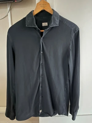 Sonrisa skjorta - Stilren mörkblå skjorta med klassisk krage och knäppning framtill. Skjortan har långa ärmar och är tillverkad i ett mjukt, tunt tyg som ger en avslappnad men ändå uppklädd look. Perfekt att matcha med jeans eller chinos.