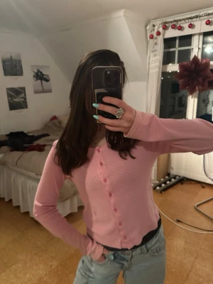 Ljusrosa cardigan med hålmönster - Söt ljusrosa cardigan med små hålmönster och knappar framtill. Tröjan har långa ärmar och en figurnära passform. Materialet är  mjukt och stretchigt , vilket gör den bekväm att bära. 