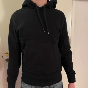 Svart CP Company hoodie - Säljer nu en snygg svart CP Company hoodie som är i grymt skick och ändast använd ett fåtal gånger. Inköpt på Thernlunds i Stockholm och nypris på denna ligger på ca 2700 kr. Personen på bilden är 177 cm och väger 65 kg. Kvitto finns! Hör av dig vid frågor!