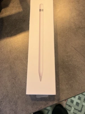 Apple Pencil digital penna - Apple Pencil är en vit digital penna med slimmad och stilren design, perfekt för att rita eller anteckna på iPad. Tillverkad i plast med en metallisk detalj vid toppen. Kommer i originalförpackning. Har tappat bort laddaren men den går och ladda på Ipade och den stora använt bara i 1 år 