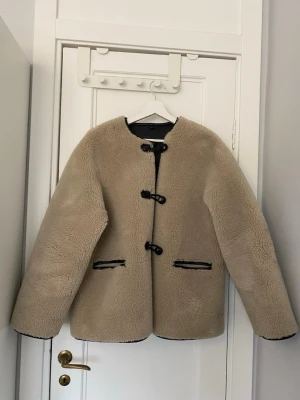 Beige teddyjacka med svarta detaljer - Säljer denna slutsålda och trendiga beiga teddyjacka ifrån Mango. Den har svarta knäppningar och svarta detaljer vid fickorna. Den har en liten fläck på en av armarna (som synd på sista bilden), men det är inget som jag tycker att man tänker på när man har på sig den. 