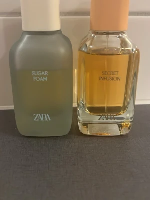 ZARA Sugar Foam & Secret Infusion parfym - Två parfymer från ZARA: Sugar Foam i en frostad, grågrön flaska med vit kork och Secret Infusion i en klar glasflaska med persikofärgad kork. Båda har modern design och stilrena etiketter. Perfekta för dig som gillar trendiga dofter.