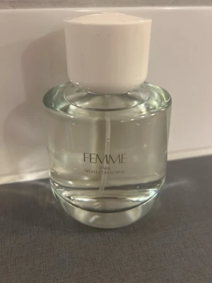 Zara Femme Night Collection parfym - Elegant parfymflaska från Zara Femme Night Collection med transparent glas och vit rund kork. Flaskan har en stilren och modern design med subtil text på framsidan. Perfekt för dig som gillar minimalistiska och snygga parfymer.