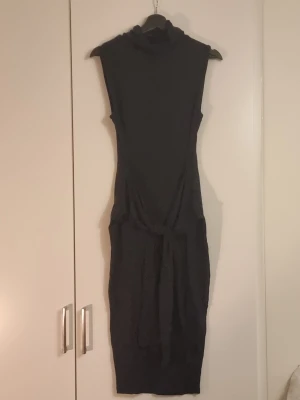 Svart ärmlös poloklänning - Snygg svart ärmlös klänning med polokrage och knytband i midjan från Missguided. Klänningen har en smal, kroppsnära passform och slutar under knäna. Perfekt för dig som gillar minimalistisk och stilren design.