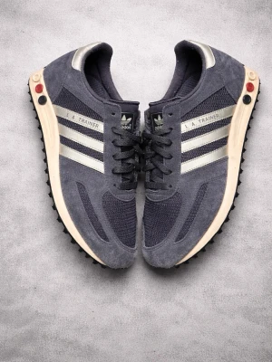 Adidas LA Trainer blå sneakers - Snygga Adidas LA Trainer sneakers i mörkblå mocka och mesh med klassiska silvriga stripes på sidorna. Skorna har retrovibbar, svart yttersula med nitar och vit mellansula. Dom här skorna säljs inte längre och är väldigt eftertraktade hör av er vid frågor och funderingar. 