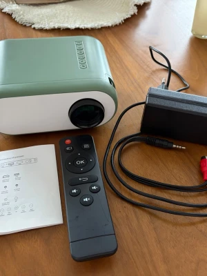 Q11 LED projektor med fjärrkontroll - Säljer en kompakt Q11 LED-projektor i grön och vit plast. Medföljer fjärrkontroll, strömadapter och manual. Projektorn har LCD-bildteknik och flera anslutningsmöjligheter. Perfekt för filmkvällar. 