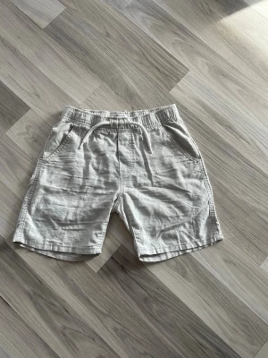 Beiga shorts med snörning från Lindex - Snygga och bekväma beiga shorts från Lindex med elastisk midja och vit snörning. Tillverkade i ett mjukt material som passar perfekt för varma dagar. Två sidofickor ger en avslappnad look.