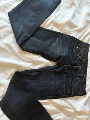 Mörkblå jeans från G-Star RAW - Säljer ett par mörkblå jeans från G-Star RAW med snygga slitningar och kontrastsömmar. Jeansen har raka ben, klassiska fem fickor och coola broderade detaljer på bakfickorna. Materialet är kraftig denim i bomull. Perfekta för en avslappnad och trendig look. Omsydda för att bli mer low rise.