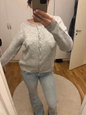 Ljusgrå knappad kofta - Mysig ljusgrå kofta med rund halsringning och knappar framtill. Koftan har långa ärmar och ribbade muddar vid ärmslut och nederkant. Perfekt för lager på lager och enkel att matcha med olika stilar.