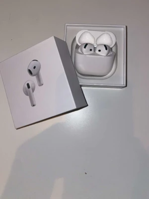 Apple AirPods med laddningsetui - Säljer ett par vita Apple AirPods med trådlöst laddningsetui. Snygg och stilren design i plast, perfekt för dig som vill ha smidiga hörlurar till mobilen. Kommer i originalförpackning med manualer.