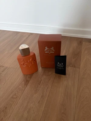 Parfums de Marly Althaïr parfym - Exklusiv parfym från Parfums de Marly, modellen Althaïr. Flaskan är matt orange med elegant reliefmönster och silverfärgat lock. Kommer med matchande orange kartong och svart booklet. Lyxig design som sticker ut i badrumshyllan.
