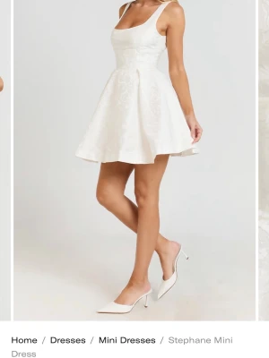 Vit kort klänning - Supersöt vit kort klänning från showpo. Klänningen har en djup urringning fram och öppen rygg, samt ett diskret blommigt mönster i tyget. Perfekt för studenten eller sommaren. Säljer då den var för liten 💕