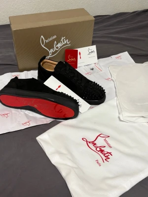 svarta Louboutins  sneakers - Svarta  Louboutins i mocka med ikoniska röda sulor och spikar. Snygg och edgy design med exklusiv känsla, perfekt för dig som vill sticka ut. Levereras med originalkartong och dustbags.