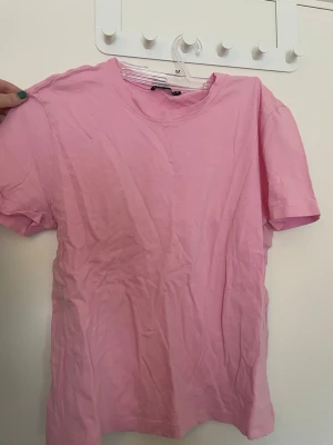 Rosa t-shirt från Zara - En enkel och stilren rosa t-shirt från Zara i mjuk bomull. Klassisk rund halsringning och korta ärmar. Perfekt basplagg att matcha med jeans eller kjol. Färgen är ljusrosa och materialet känns skönt mot huden. Den är liten i storlek.