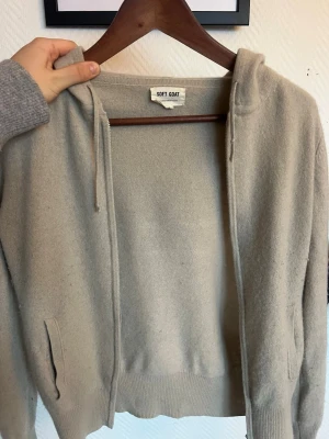 Beige hoodie i kashmir från Soft Goat - Mysig beige hoodie från Soft Goat i 100% kashmir. Hoodien har dragkedja framtill, två fickor och justerbar huva med snören. Perfekt för dig som gillar stilrena och bekväma plagg med lyxig känsla. Passar till allt och är superenkel att matcha.