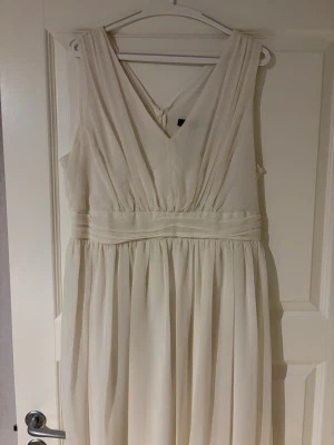 Vit kortklänning med v-ringning - Elegant vit kortklänning med v-ringad fram- och baksida samt markerad midja. Klänningen har ett fint fall och är ärmlös, perfekt för sommarens tillfällen. Tillverkad i ett lätt och luftigt material som ger en mjuk känsla.