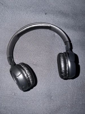 Svarta on-ear hörlurar från JBL - Snygga svarta on-ear hörlurar från JBL med vadderade öronkuddar i konstläder och justerbart huvudband. Perfekta för musik, gaming eller videos. Trådlös design och stilren look med JBL-logga på båda sidor.