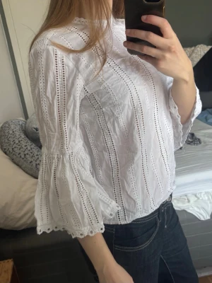 Vit broderad blus med spetsdetaljer - Söt vit blus med broderade spetsdetaljer och lodräta hålmönster. Blusen har rund halsringning och trekvartsärmar med volangkant. 