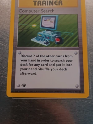 Computer Search 1st Edition  - Säljer ett Pokémonkort av typen Trainer med namnet Computer Search. Kortet har en bild på en retro dator och text på engelska om spelets funktion. Baksidan har den klassiska blå Pokémon-designen med en Pokéboll i mitten.
