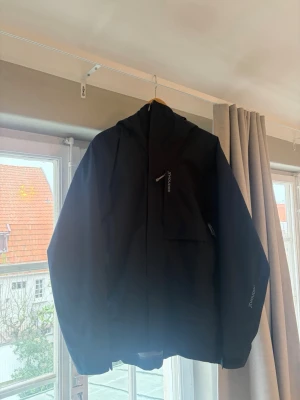 Marinblå skidjacka från Houdini  - Snygg mörkblå skidjacka från houdini med huva och dragkedja framtill. Jackan är i väldigt gott skick använd 1 semester. Modellen är rollercoaster.