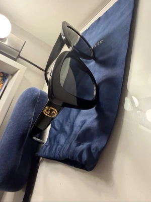 Gucci solglasögon  - Säljer mina fina solglasögon från Gucci i klassisk cat eye-modell. Glasögonen har breda bågar i blank plast och guldigt GG-logo på sidorna. .