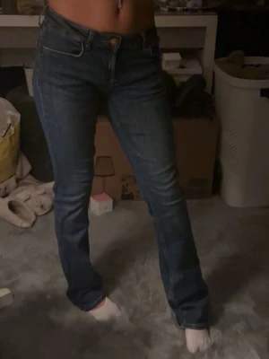 Mörkblå låga bootcut jeans - Säljer ett par mörkblå bootcut jeans med klassisk femficksdesign och normal midja. Jeansen har en lätt utsvängd passform nedtill och är tillverkade i denim med snygga kontrastsömmar. Perfekta för en avslappnad och trendig look.