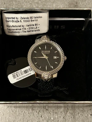 Versus Versace silverfärgad herrklocka - nyskick - Snygg klocka från Versus Versace med silverfärgat boett och svart urtavla. Klockan har ett detaljerat lejonmotiv och datumvisning. Armbandet är svart och har en texturerad yta som ger en cool look. Perfekt accessoar för dig som vill sticka ut.  Säljes p.g.a. behov av pengar. Priset kan diskuteras vid snabb affär.