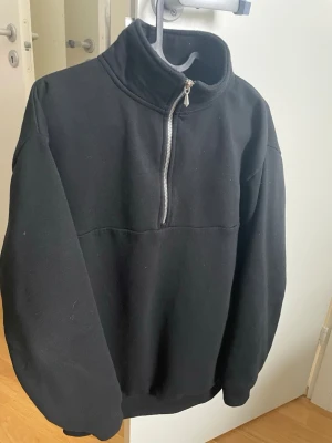 Svart halvzip tröja från SMOG - Svart relaxed fit tröja från SMOG i storlek XS. Tröjan har hög krage och halv dragkedja framtill. Perfekt för en avslappnad och stilren look. Tillverkad i mjukt material som känns skönt mot huden.