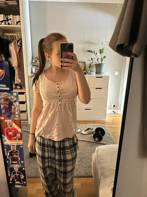 Ljusrosa kortärmad topp med knappar - Ljusrosa topp med rund halsringning och korta ärmar. Toppen har dekorativa knappar framtill och ett lätt rynkat parti under bysten som ger en feminin och avslappnad passform. Materialet ser ut att vara mjukt och bekvämt, troligen bomull.