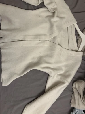 Beige ribbad kofta med knäppning - Säljer en stilren beige kofta med diskret ribbad struktur och knäppning framtill. Koftan har långa ärmar och en mjuk, lätt stretchig känsla. Perfekt att slänga över en t-shirt eller topp för en enkel look.