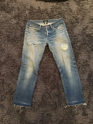 Blå slitna jeans från A.P.C. - Säljer ett par blå jeans från A.P.C. med slim fit och slitningar på båda benen. Jeansen har råa benslut och klassisk femficksmodell. Materialet är denim i bomull och färgen är tvättad blå med ljusare partier och distressed detaljer. Mått och bild på skickas vid intresse!🤩